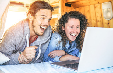 Happy man and woman watching surprised on their computer - Travel couple using laptop during their journey on a vintage minivan with wood interior - Vacation, love, technology concept