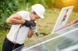 © anatoliy_gleb - Profile of professional technician working with screwdriver connecting solar photo voltaic panel to metal platform on green summer blurred bokeh background. Alternative sun energy production concept.
