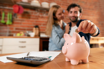 Wall Mural - Happy couple inserting coin in piggybank