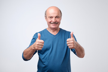 Wall Mural - Handsome senior man in blue shirt shows thumb up. He is satisfied with advice