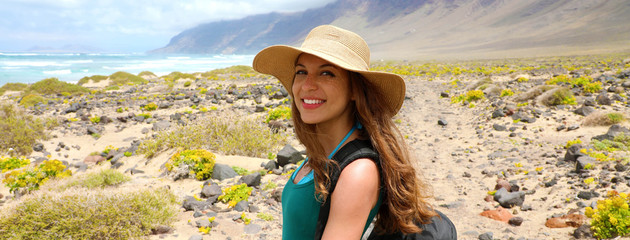 Wall Mural - Happy beautiful traveler girl with straw hat looking to the camera. Young female backpacker exploring Lanzarote, Canary Islands. Banner panorama.