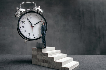 Businessman stands on stairs and tries to change clock hand position. Surrealistic conception of time problem in business.