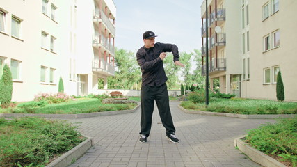 A young man dressed in black breakdancing in the street. Long shot