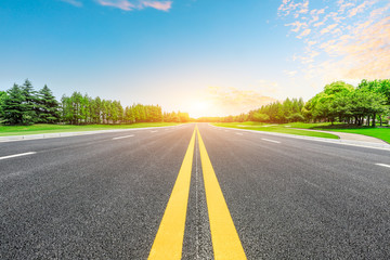 Empty asphalt road and green forest with colorful clouds at sunset