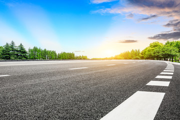 Empty asphalt road and green forest with colorful clouds at sunset