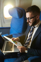 Wall Mural - High angle portrait  of smiling bearded businessman working while enjoying flight in first class, copy space