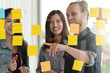 © ChayTee - Group of young successful creative multiethnic team smile and brainstorm on project together in modern office with post note or sticky note. Caucasian man point on glass wall sharing idea.