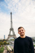 © Aleksandr - Cheerful man tourist in dark blue pullover is standing on the background of the Eiffel Tower