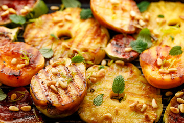 Grilled fruits; pineapples, peaches, figs, pears and watermelon with pine nuts, fresh herbs and honey on the grill plate, close-up. Gourmet fruit dessert