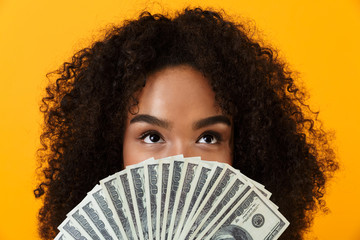 Woman posing isolated over yellow background holding money covering face.