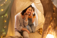 Family, Hygge And People Concept - Happy Mother With Little Daughter Whispering In Kids Tent At Night At Home