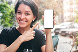Fototapeta Koty - Happy beautiful woman holding and showing mobile phone with blank white screen in cafe