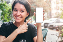Happy Beautiful Woman Holding And Showing Mobile Phone With Blank White Screen In Cafe