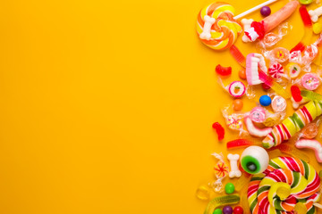 Wall Mural - Assorted teeth & eyeball shaped candy spread on yellow background, jelly spider, gummy worms, sugar bones, round lollipop and other mixed candy, bloody finger. Top view, copy space, close up, flat lay