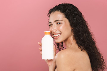 Sticker - Smiling beautiful young woman posing isolated over pink background take care of her skin holding cream lotion gel.