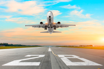 Airplane flying deperture take off on a runway in the evening during a bright red sunset.