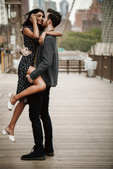 Love story in New York. Man and exotic woman dance with passion on the street with Brooklyn bridge behind them