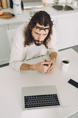 Canvas Print - high angle view of Jesus eating corn flakes on breakfast at table with laptop in kitchen at home