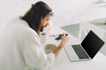 Wall Mural - side view of Jesus eating corn flakes on breakfast at table with laptop in kitchen at home