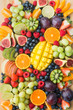 Assortment of healthy raw fruits and berries platter background, strawberries raspberries oranges plums apples kiwis grapes blueberries, mango, top view, vertical, selective focus