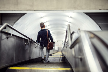 Wall Mural - Rear view of hipster businessman walking down the stairs in subway, travelling to work.