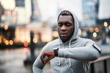 Poster - Black man runner with smartphone in an armband on the bridge in London, resting.