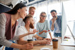 © opolja - Discussing successful project. Group of young cheerful business people working and communicating while sitting at the office desk together with colleagues sitting in the background.