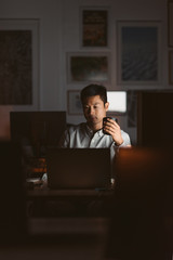 Wall Mural - Asian businessman drinking coffee while working in a dark office