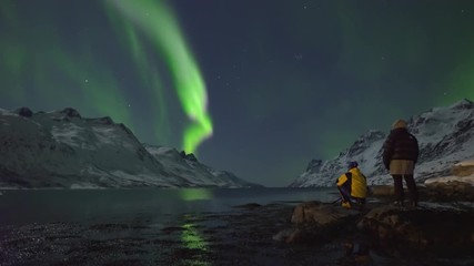 northern lights (aurora borealis) filmed in real time. two tourists photographers take pictures and 