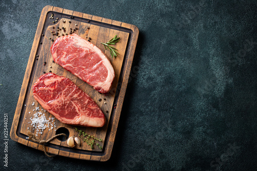 Fotomural Fresh raw Prime Black Angus beef steaks with spices on wooden board: Striploin, Rib Eye