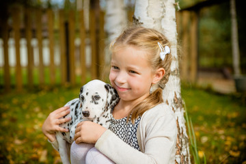 Little cute blonde girl playing with her Dalmatian puppy outdoo, on sunny warm autumn day.care of Pets concept. Child kisses,hugging her dog, the concept of children's and dog emotions, of friendship