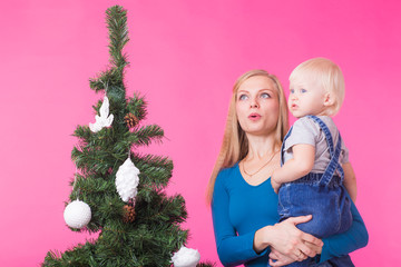 Holidays and people concept - Woman and her kid near christmas tree on pink background