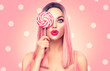 Beauty sexy model woman with trendy pink hairstyle and beautiful makeup holding lollipop candy, on pink polka dots background