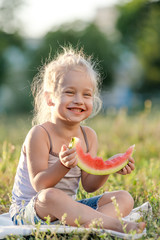 Wall Mural - Little blond girl eating watermelon in the park.