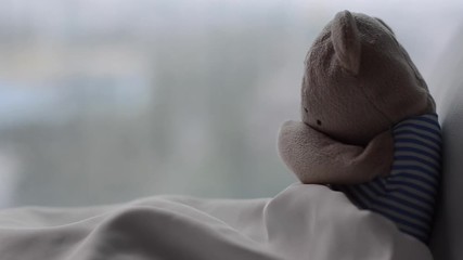 Wall Mural - HD Footage of teddy bear crying alone on bed with his white pillow and blanket near by window with rain drop in morning of the sadness day.