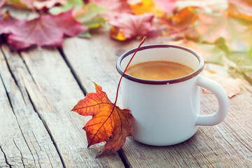 enameled cup of coffee and fallen maple leaves on wooden board.