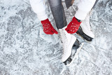 Girl tying shoelaces on ice skates before skating on the ice rink, hands in red knitted gloves.