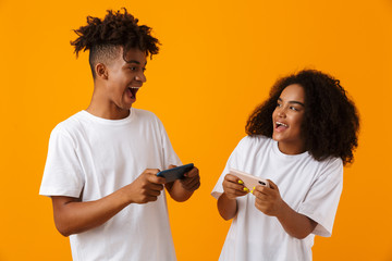 Poster - Excited young cute african couple isolated over yellow background play games by mobile phones.