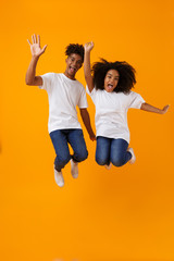 Wall Mural - Cute african couple jumping isolated over yellow background.