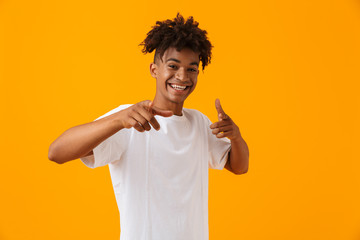 Happy young african man posing isolated over yellow background pointing.