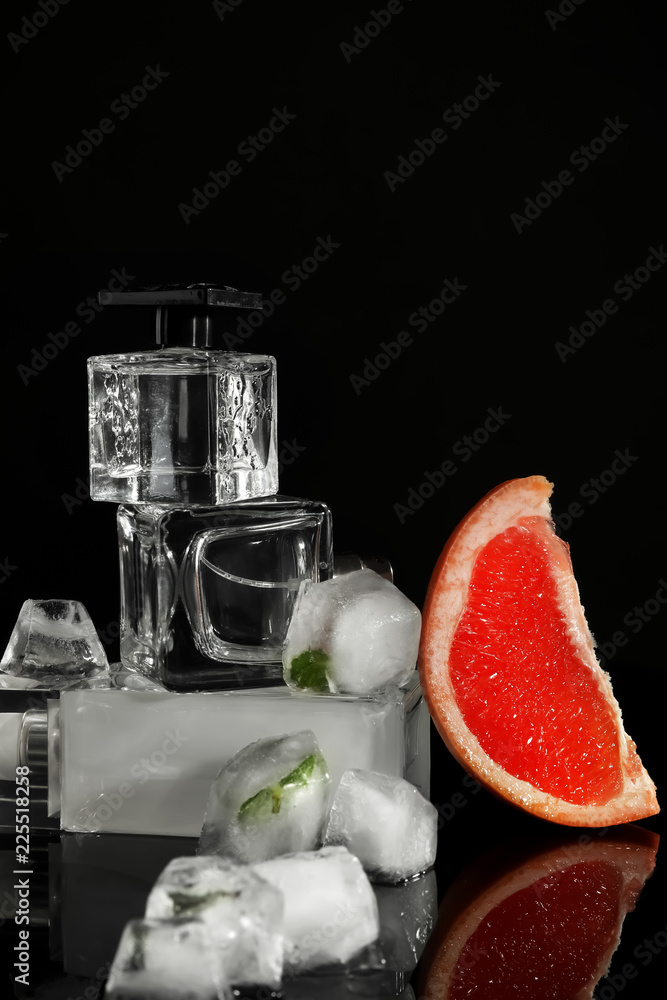 Bottles with perfume, piece of grapefruit and ice cubes on black background