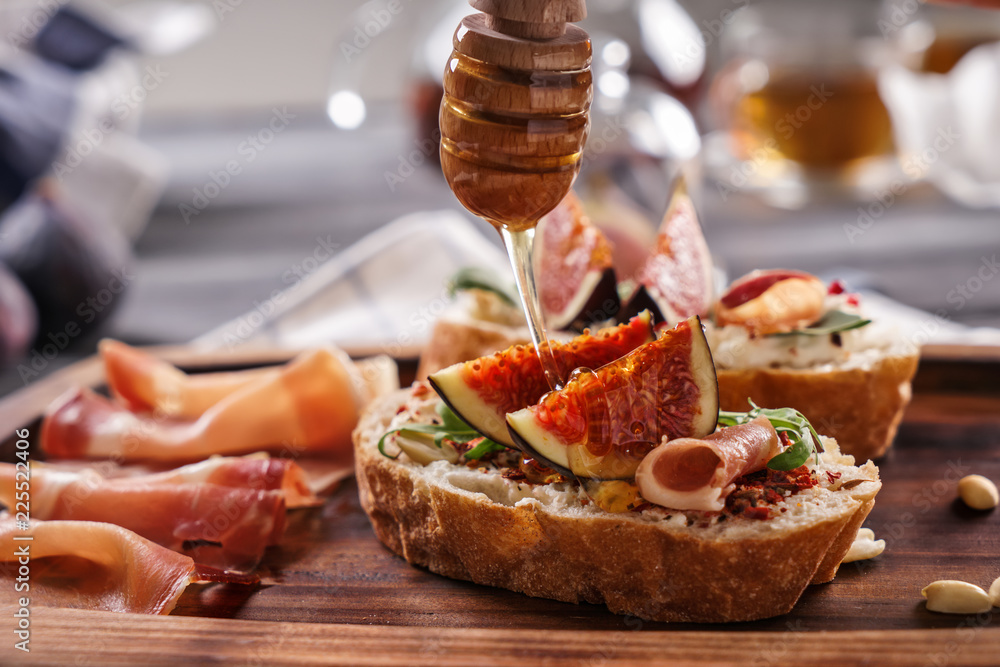 Sweet honey dripping from dipper onto sandwich with ripe fig