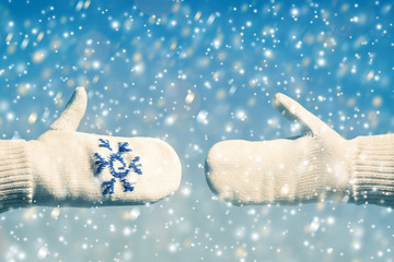 Gestures of hands in the winter mittens on the snowfall background