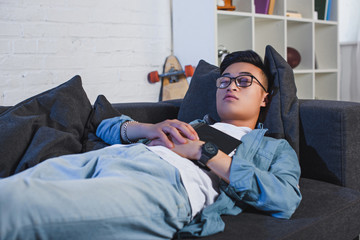 Wall Mural - young asian man in eyeglasses holding book and sleeping on couch