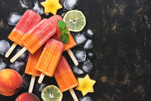 Peach popsicles with ice cubes on a rustic dark background. Top view, space for text.