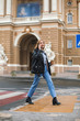 © Anton - Young attractive woman in leather jacket and jeans holding cup of coffee to go in hand talking on cellphone while dreamily walking on cozy city street