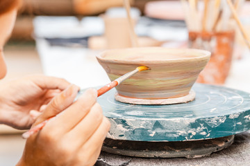 Wall Mural - A woman artist in working apron paints a clay pottery among brushes and other tools in the modern workshop