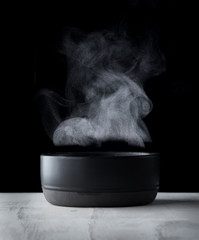 Steam of hot water in a bowl with smoke over dark background