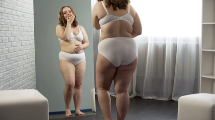 Wall Mural - Happy fat girl admiring mirror reflection, eating sweet donuts, body positive