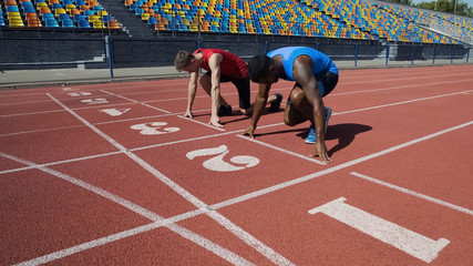 Two multiracial athletes in starting position, ready to run after command